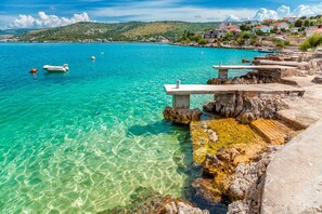 A coastal scene with clear turquoise waters, rocky outcrops, and a few boats. - Spacious apartment with balcony, big garden & grill, near beach (Podglavica)