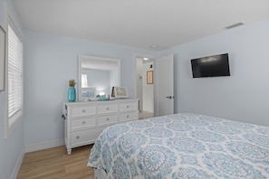 A bedroom with a bed, dresser, mirror, and a television on the wall. - Lucky 307- 3 bedroom with pool and spa- Managed by Beach House Real Estate (Holmes Beach)