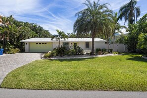 A single-story house with a garage, surrounded by a well-maintained lawn and palm trees. - Lucky 307- 3 bedroom with pool and spa- Managed by Beach House Real Estate (Holmes Beach)