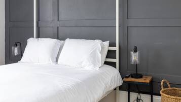 A bedroom with a four-poster bed, two bedside lamps, a bedside table with a lamp, and a woven basket.