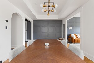 Un salón de conferencias con una mesa de madera, una araña y una pared de paneles grises.