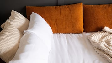 Una cama con ropa de cama blanca y dos almohadas anaranjadas.