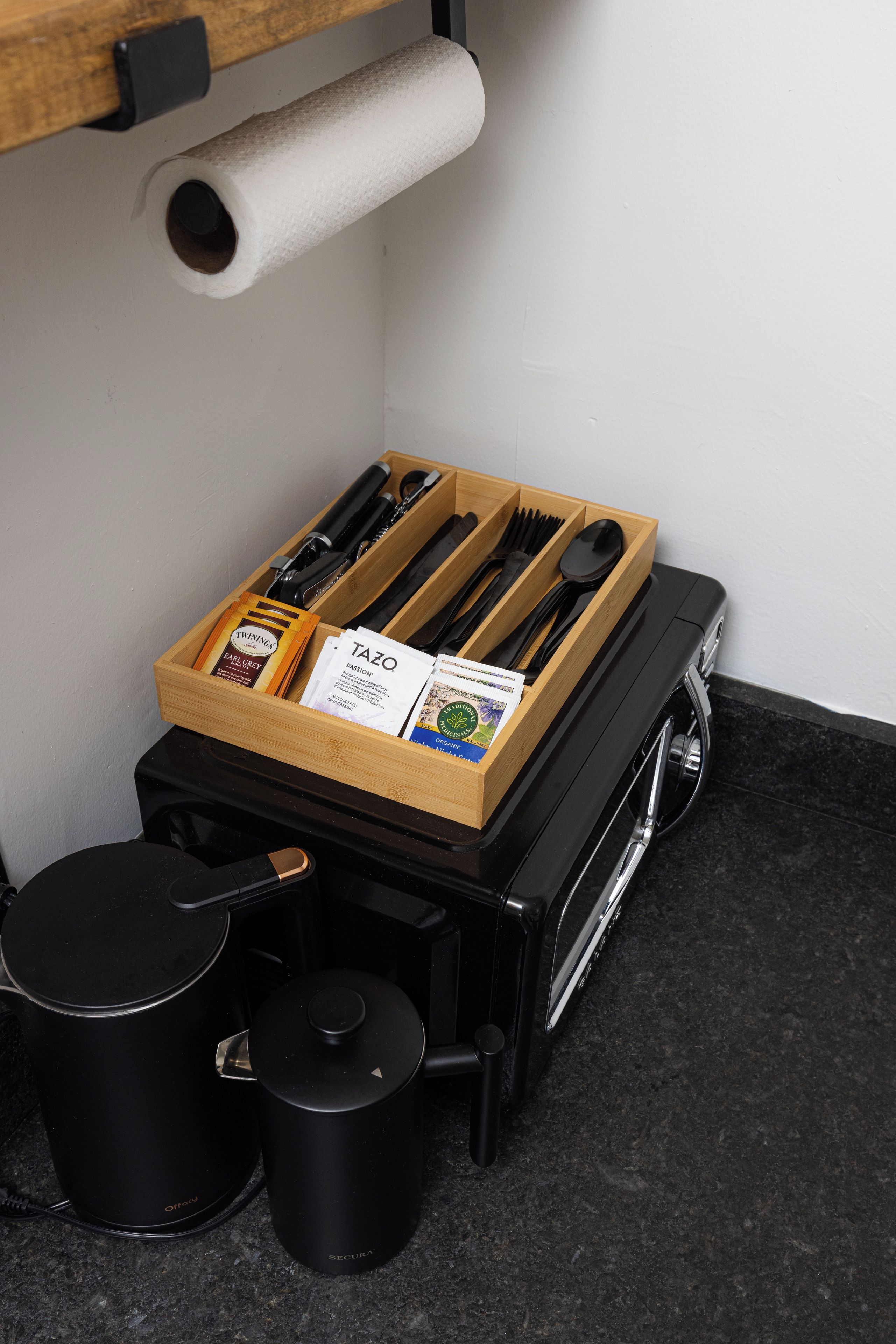 A kitchen area with a wooden utensil organizer, a black coffee maker, and two black containers.