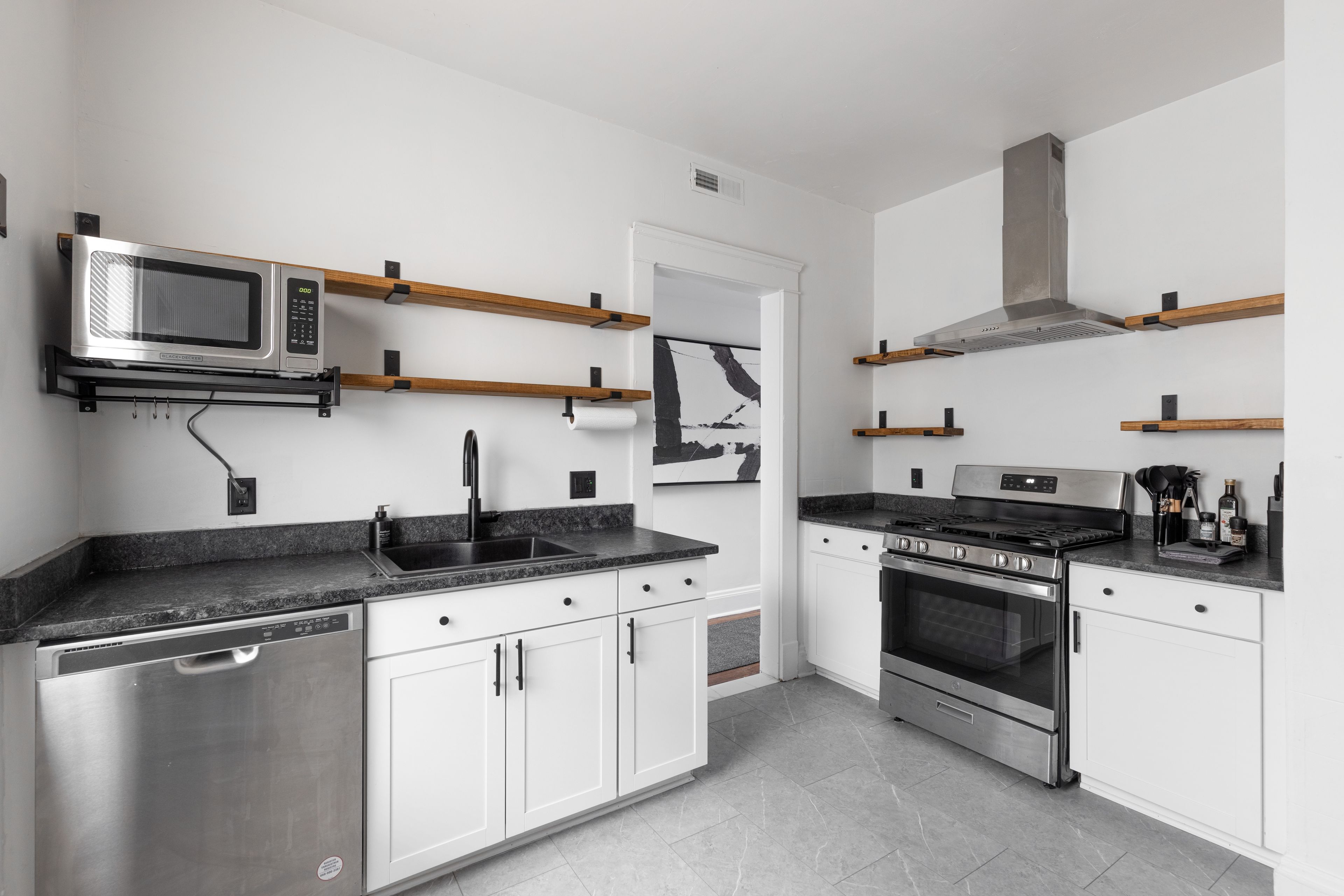 A modern kitchen with stainless steel appliances, wooden shelves, and a tiled backsplash.