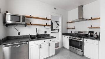 A modern kitchen with stainless steel appliances, wooden shelves, and a tiled backsplash.