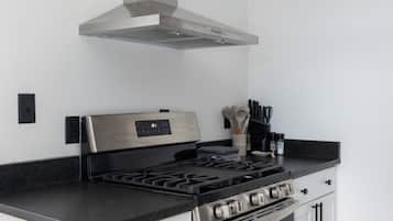 A modern kitchen with a stainless steel stove, white cabinetry, and a range hood.