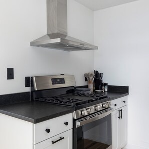 A modern kitchen with a stainless steel stove, white cabinetry, and a range hood.