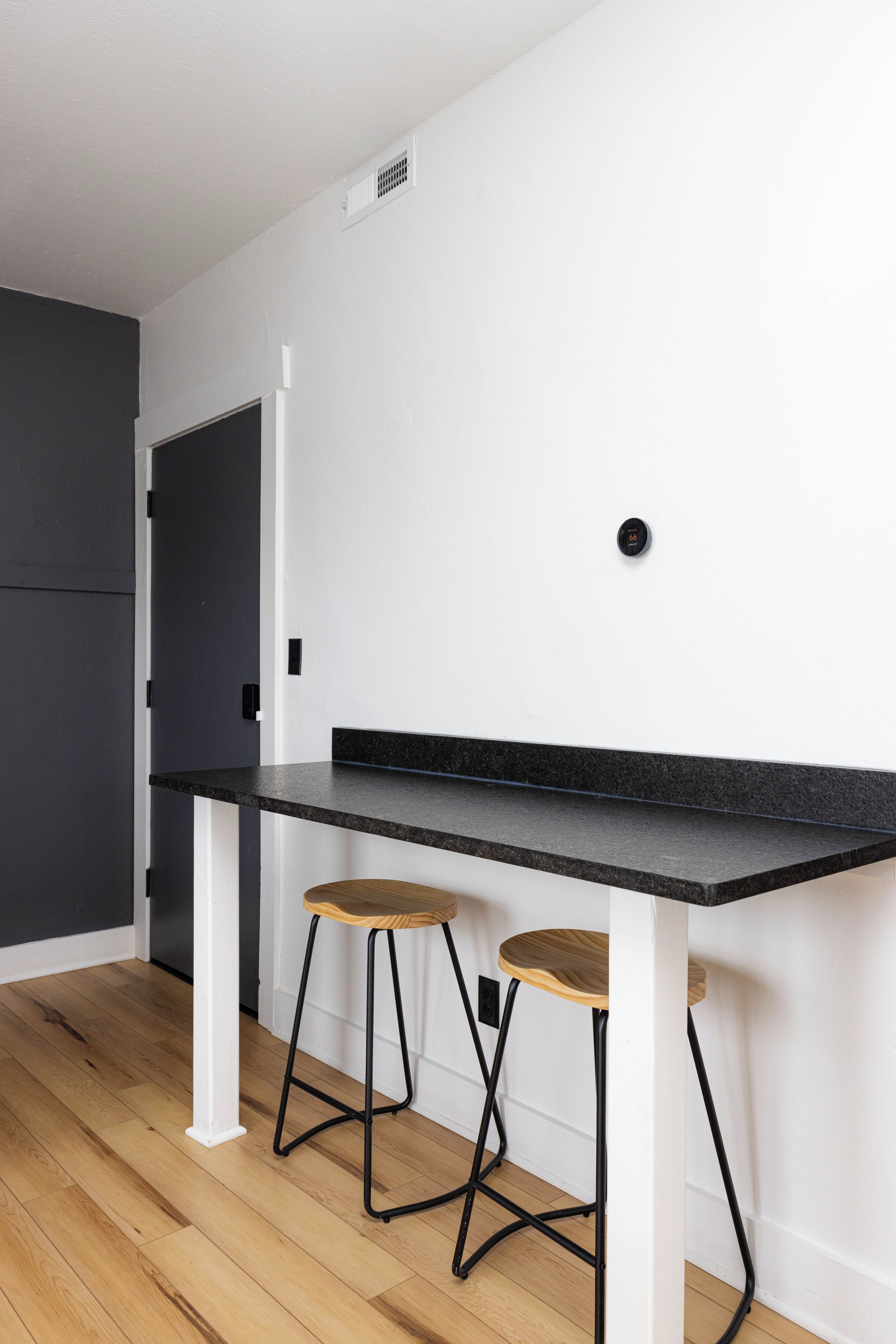 A kitchen with a black countertop, two wooden stools, and a white door.