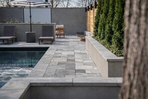 Un área junto a la piscina con solárium de baldosas, sillas de descanso y una piscina pequeña.