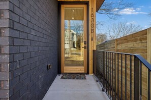 A modern building entrance with a glass door, a wooden number plaque, and a metal railing. - Nashville home with game room and home theater! (Nashville)