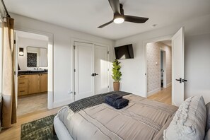 Ein Schlafzimmer mit einem Bett, einem Deckenventilator, einem an der Wand montierten Fernseher und einer Zimmerpflanze.