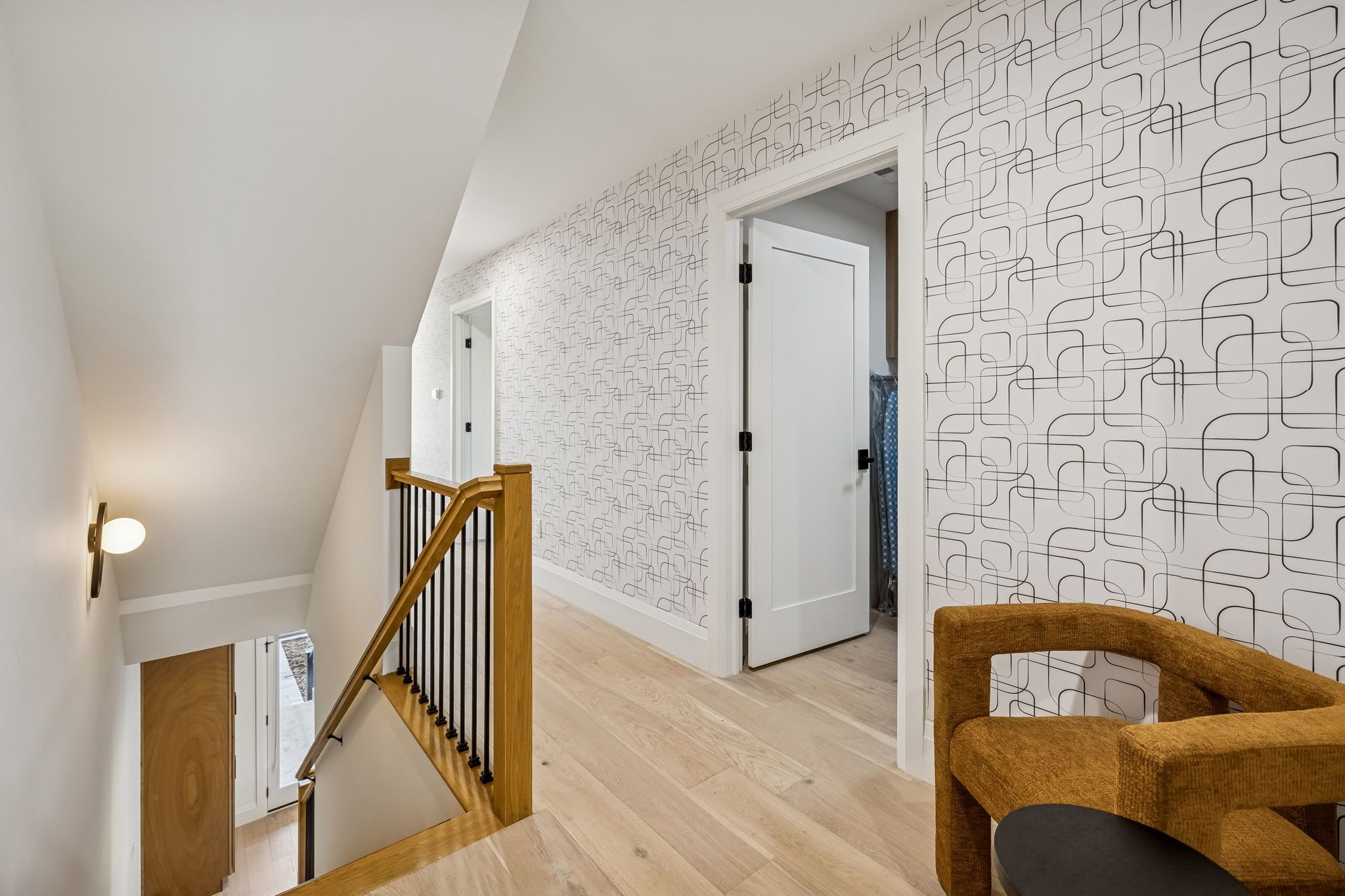 A modern interior with a wooden staircase, geometric patterned wallpaper, and a wooden chair.