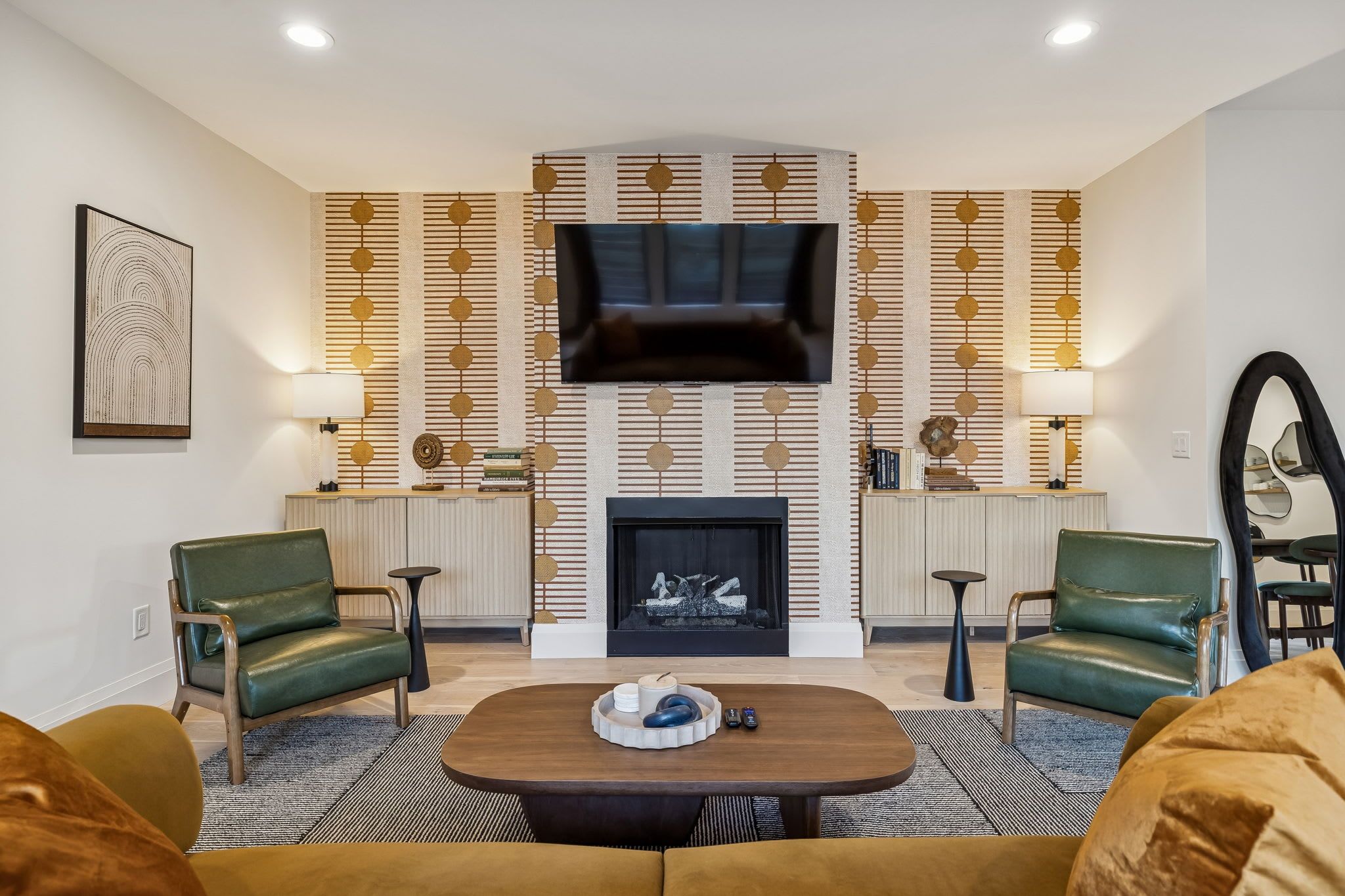 A modern living room with a fireplace, green leather chairs, a coffee table, and a TV mounted on the wall.