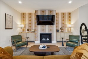 A modern living room with a fireplace, green leather chairs, a coffee table, and a TV mounted on the wall. - Nashville home with game room and home theater! (Nashville)