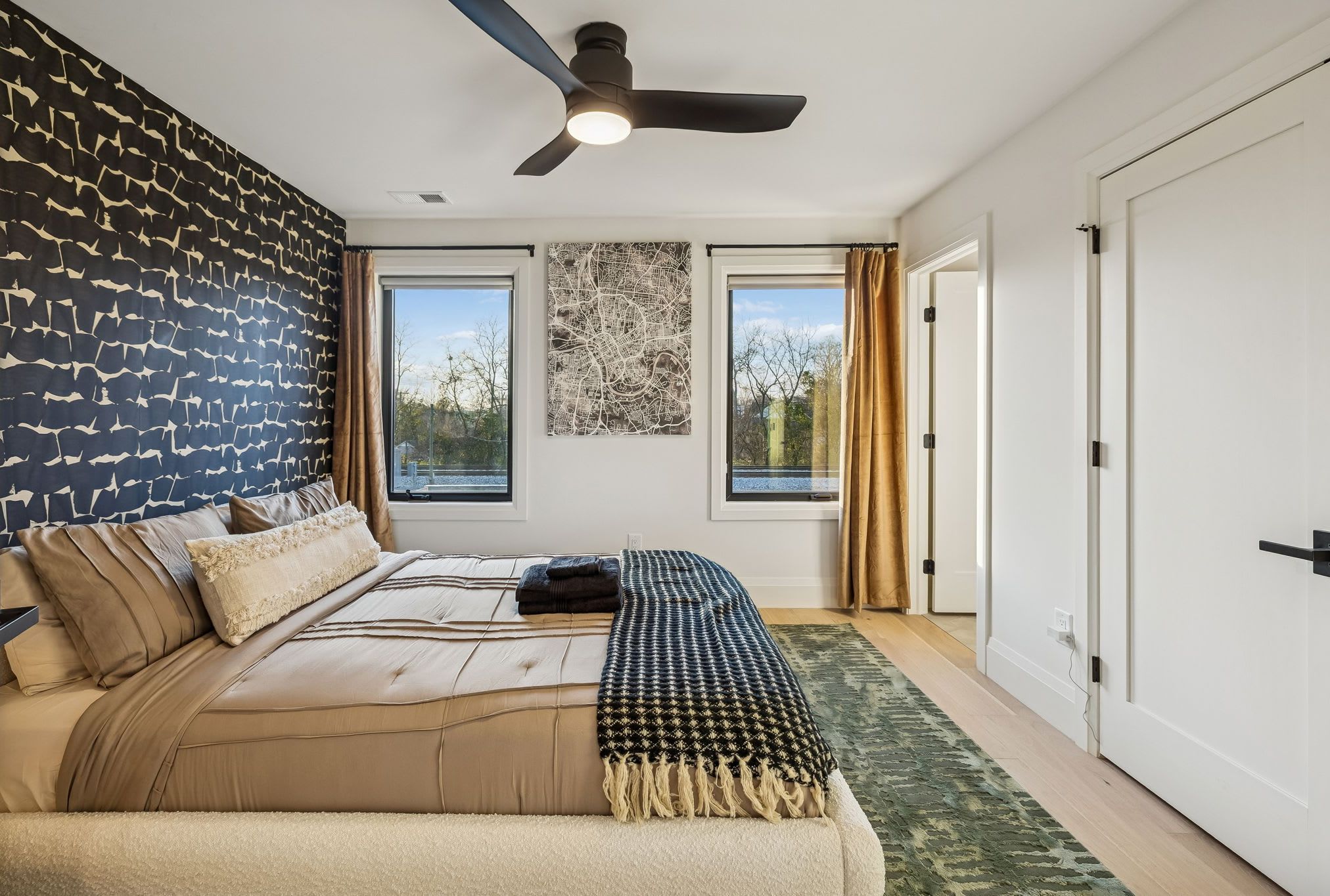 A bedroom with a large bed, a ceiling fan, and two windows with curtains.