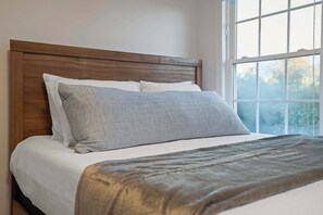 A bed with a wooden headboard, white bedding, and a grey pillow. - Lake Views, Soaking Tub, Ping Pong Table, Firepit (Sharps Chapel)