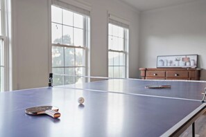 A ping pong table with a ball and paddles, large windows, and a wooden cabinet with a picture. - Lake Views, Soaking Tub, Ping Pong Table, Firepit (Sharps Chapel)