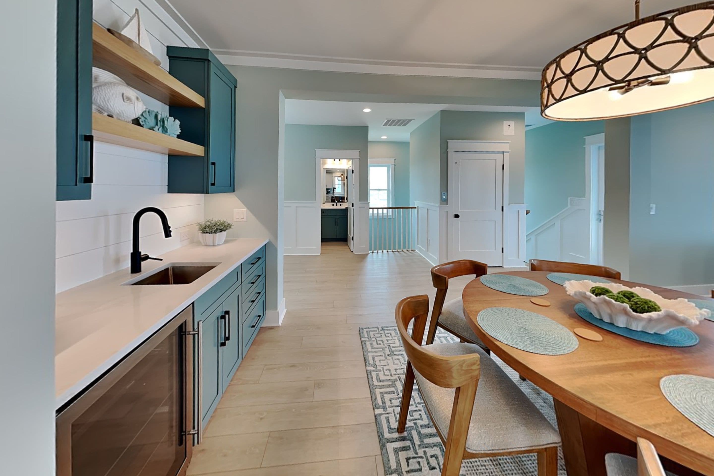 A modern kitchen with teal cabinetry, a wooden dining table, and a patterned rug.