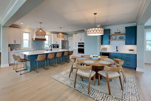 A modern kitchen with a central island, bar stools, pendant lighting, and a dining area with a patterned rug. - Klose Enough (Kure Beach)
