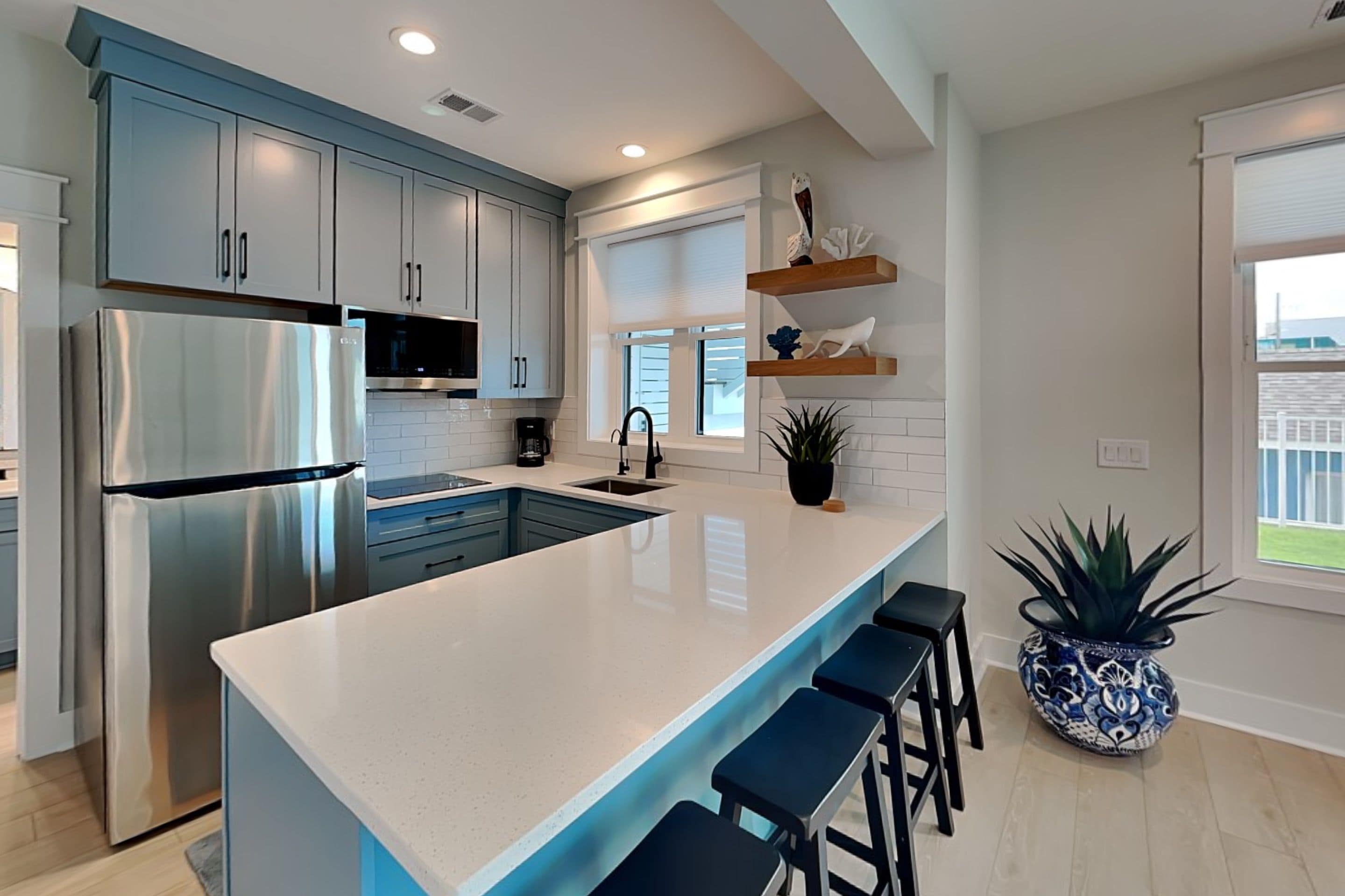A modern kitchen with a large island, stainless steel appliances, and a potted plant.