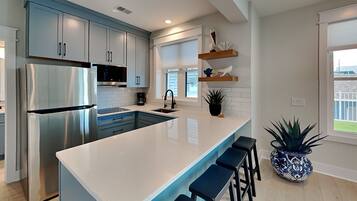 A modern kitchen with a large island, stainless steel appliances, and a potted plant.