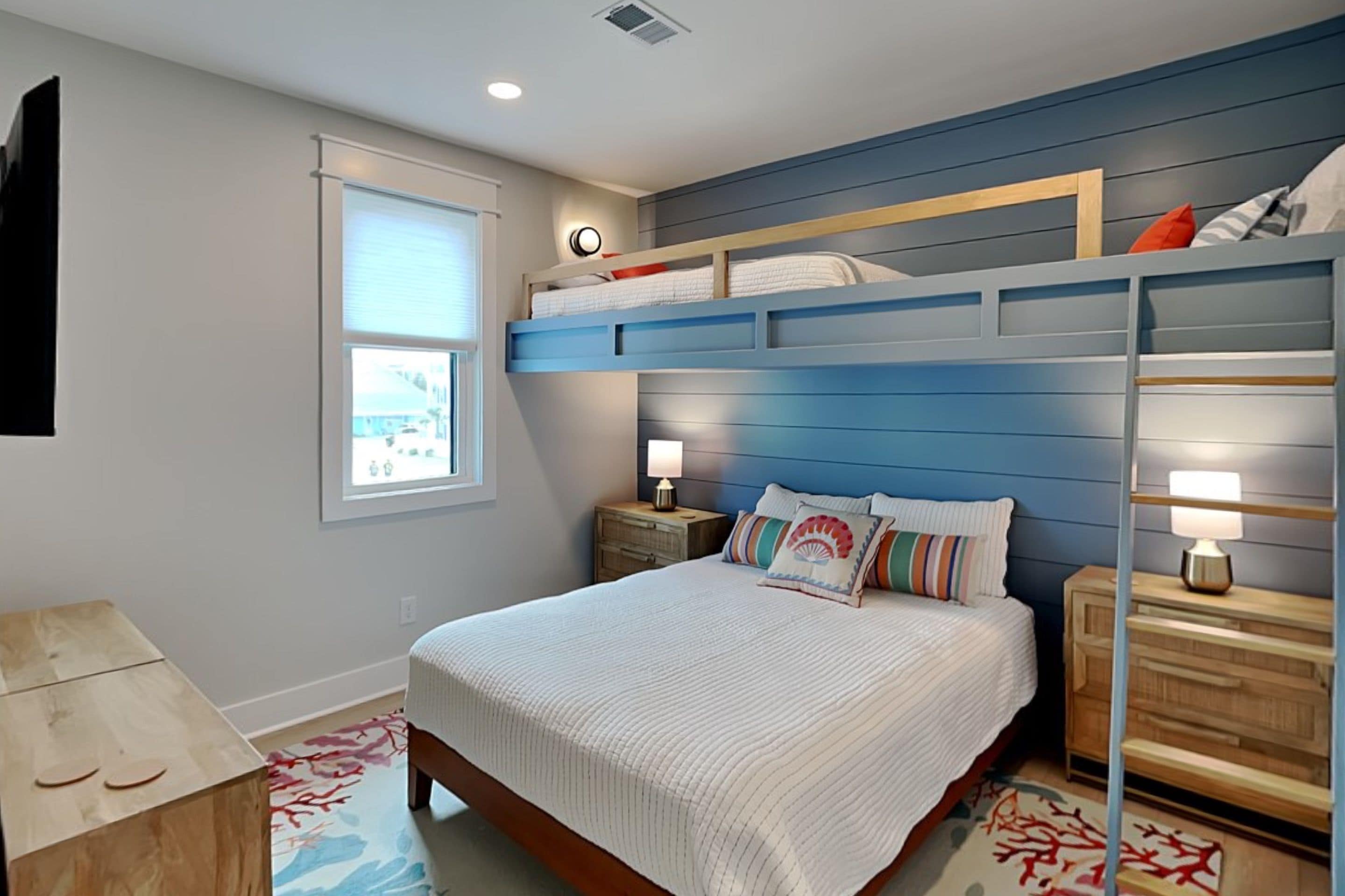 A bedroom with a bunk bed, a bedside table with a lamp, a window with blinds, and a wall clock.