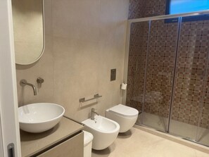A modern bathroom with a large sink, bidet, toilet, and a glass-enclosed shower area.