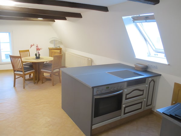 Una cocina moderna con horno empotrado, una zona de comedor con una mesa redonda y sillas, y un tragaluz.