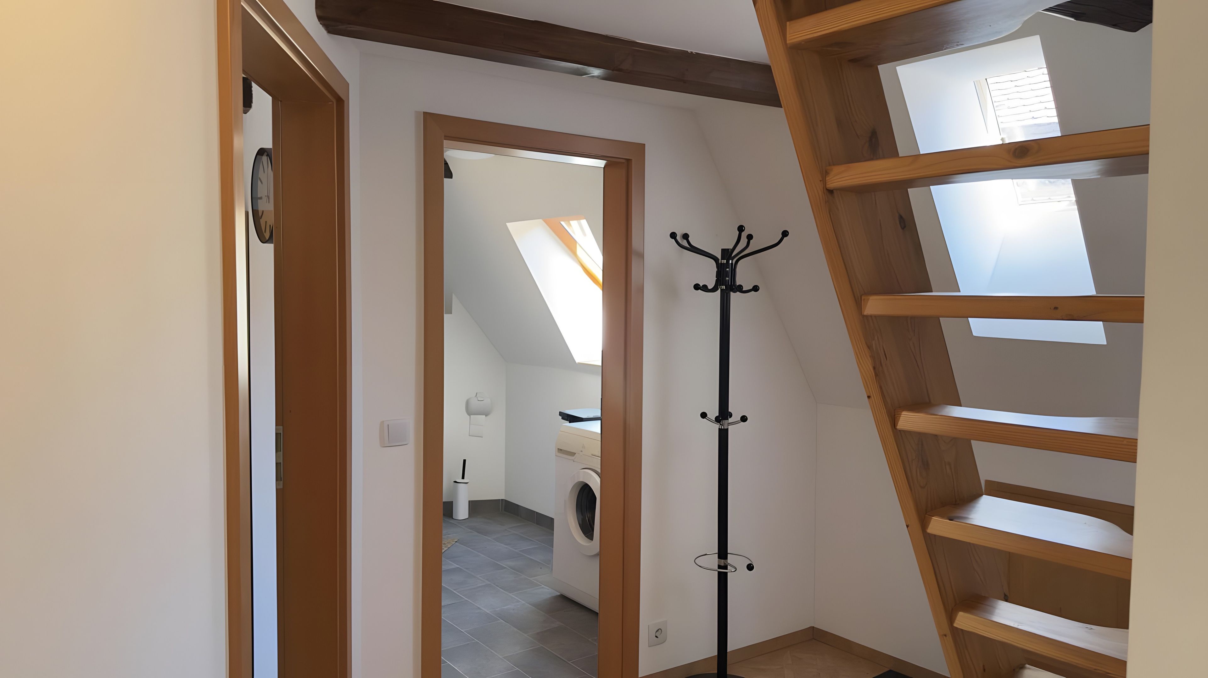 Ein Zimmer mit einer Holztreppe, einem Kleiderständer und einem Waschbereich mit einer Waschmaschine.