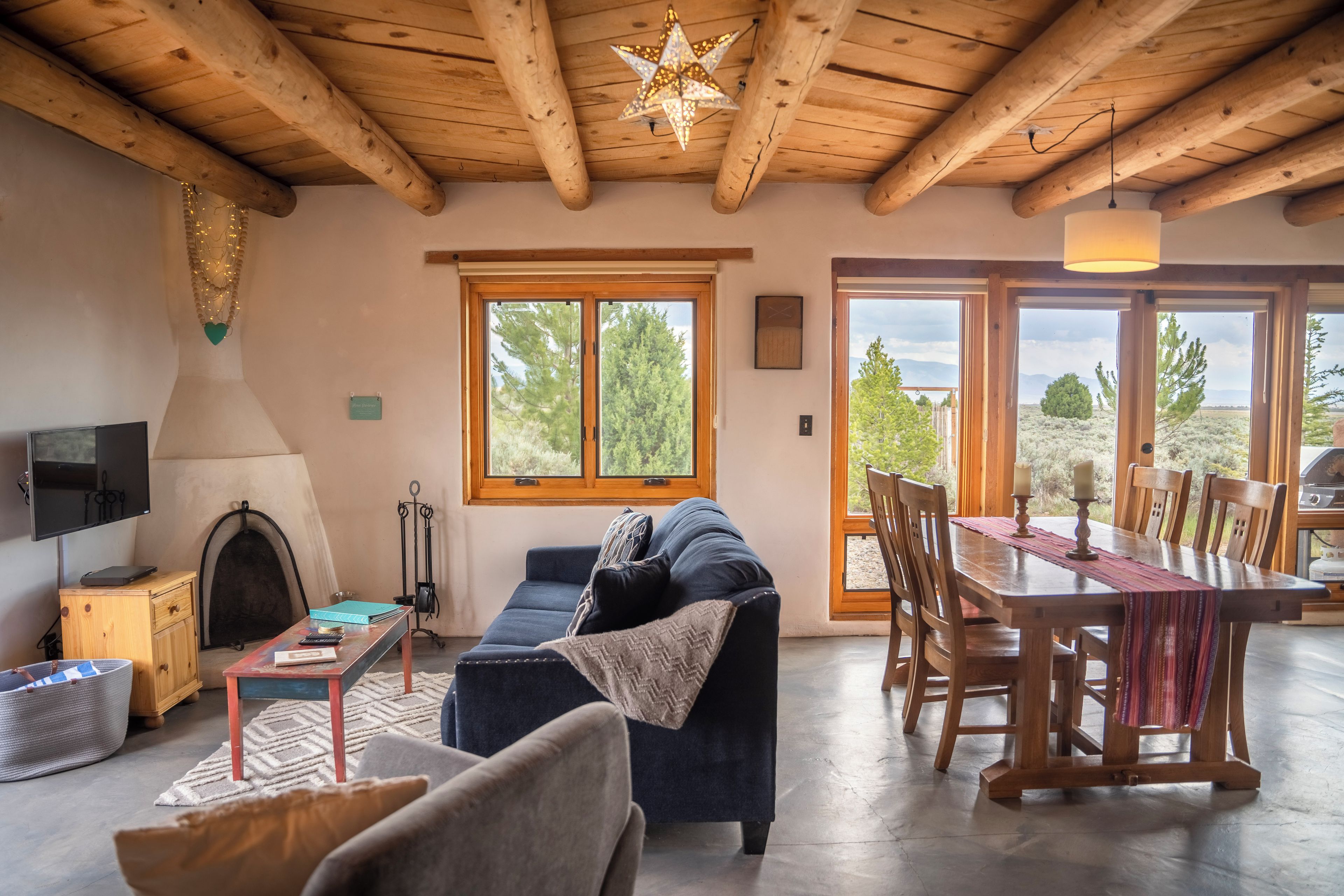 Una sala de estar acogedora con chimenea, un sofá, una mesa de comedor con sillas y ventanas amplias que ofrecen vistas al exterior.