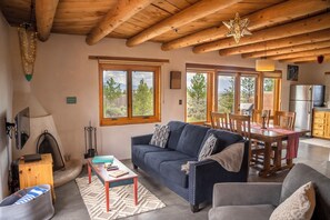 A cozy living room with a fireplace, a sofa, a dining table, and a kitchen area visible through the windows. - Casa Lobo in Arroyo Seco (El Prado)