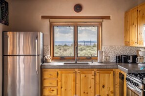 A kitchen with wooden cabinets, a stainless steel refrigerator, a window with a view, and a stove. - Casa Lobo in Arroyo Seco (El Prado)