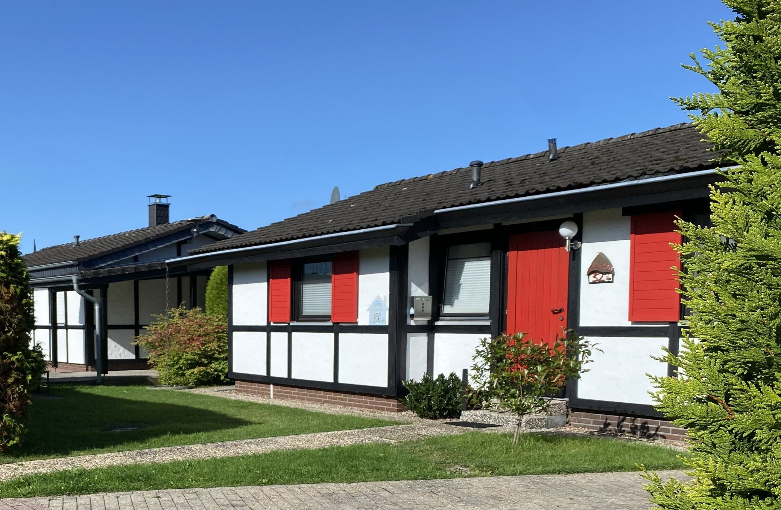 A row of two-story buildings with red shutters and white walls, featuring a clear blue sky.
