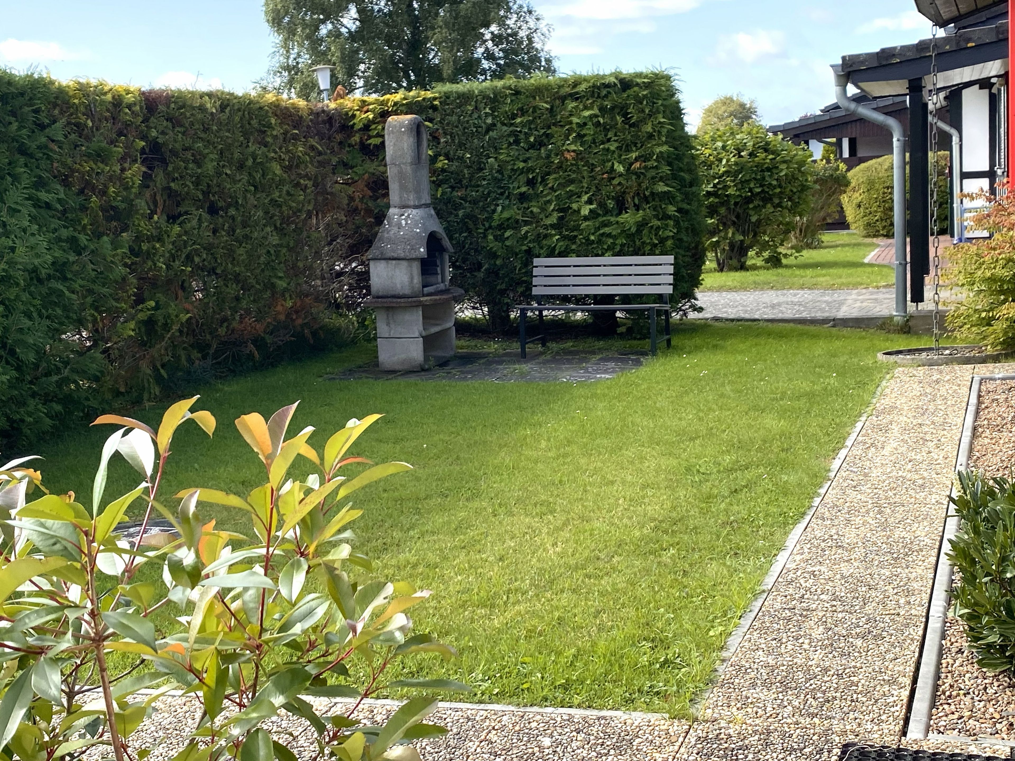 Ein gepflegter Garten mit einer Bank, einer Steinstruktur und einer Hecke.