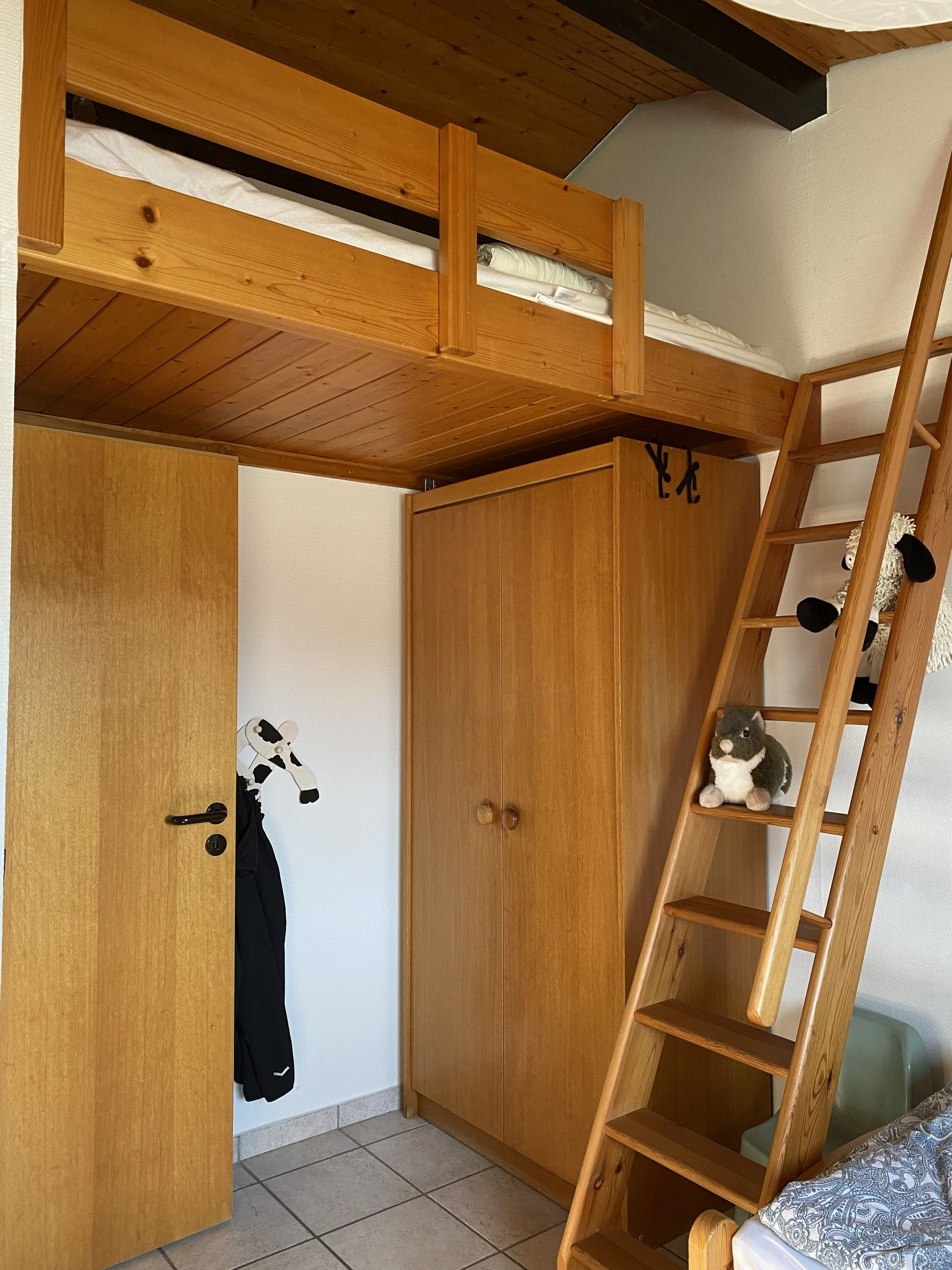 Une pièce avec une armoire en bois, une échelle et une petite étagère sur laquelle est posé un jouet en peluche.