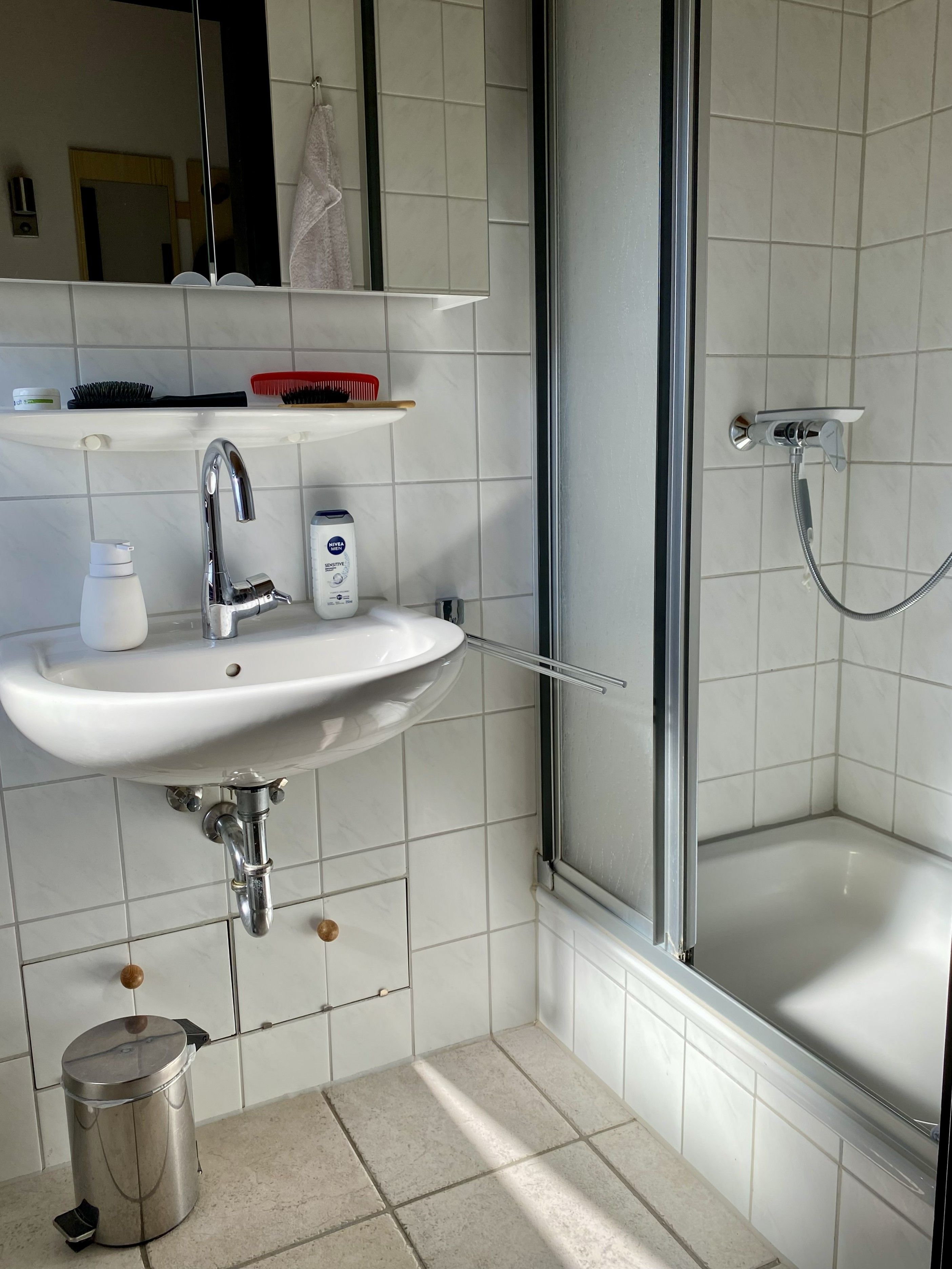 Ein Badezimmer mit Waschbecken, Spiegel, Dusche und Mülleimer.