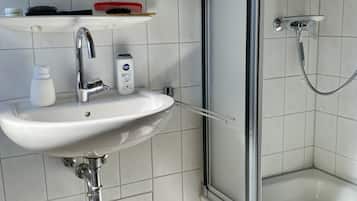 Ein Badezimmer mit Waschbecken, Spiegel, Dusche und Mülleimer.