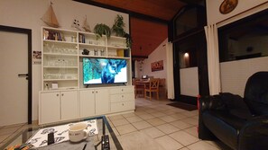 A living room with a television, shelves with various items, a coffee table with a cup, and a couch. - Holiday Home 'Haus Schöpshuus' with Wi-Fi (Butjadingen)
