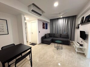 A modern living room with a sectional sofa, a dining table with chairs, a small side table, a flat-screen TV mounted on the wall, and a ceiling fan. - Finland II-1BHK_Hiranandani Estate_Spacious (Thane)