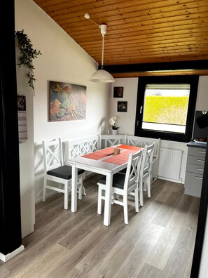 A dining area with a table and chairs, a ceiling fan, a window with a view of greenery, and a wall with artwork. - Holiday Home '"Marschenhuus"' with Wi-Fi (Butjadingen)