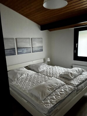 A bedroom with a bed, white bedding, a headboard, and three wall-mounted pictures. - Holiday Home '"Marschenhuus"' with Wi-Fi (Butjadingen)