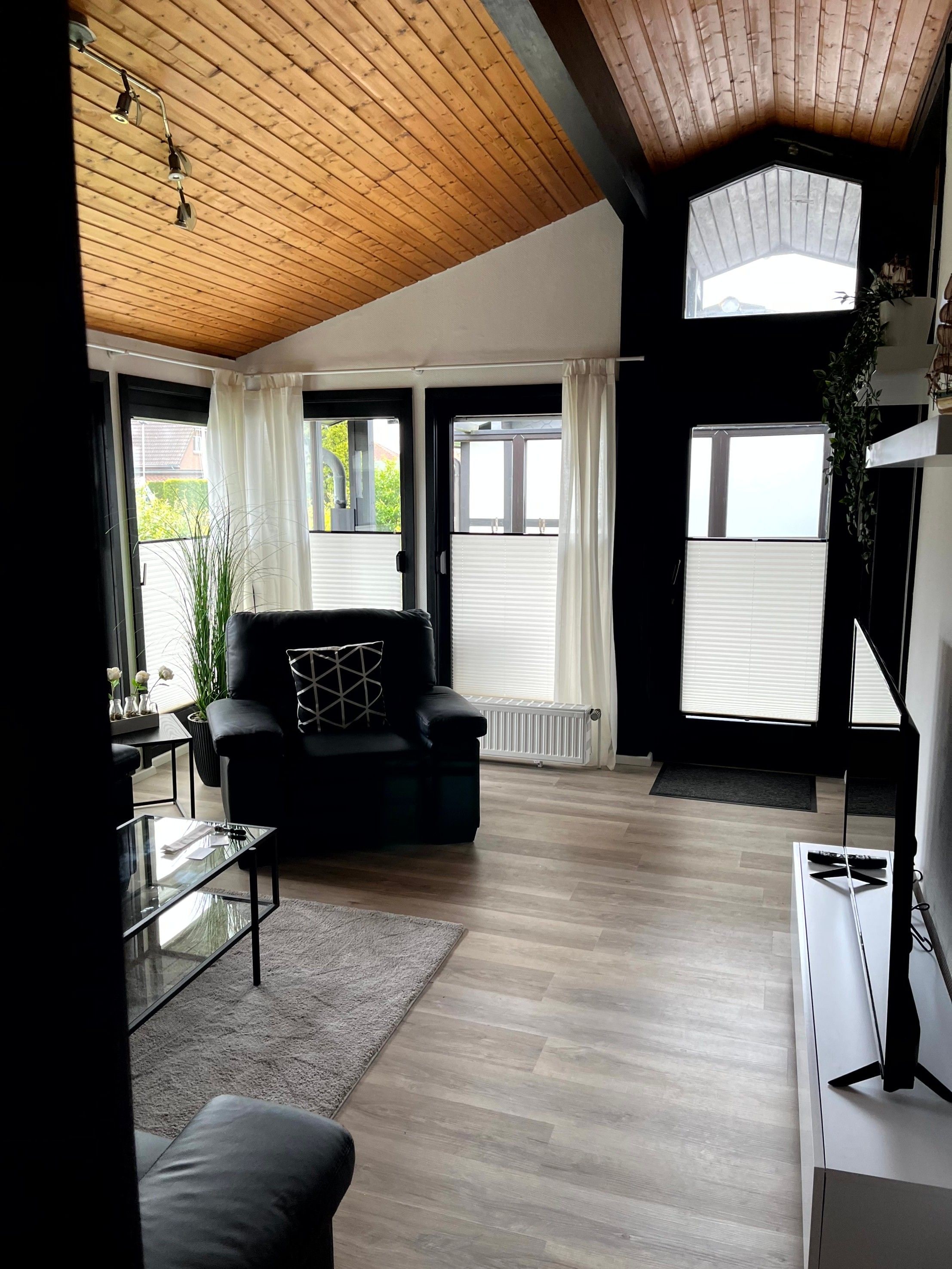 A modern living room with a black leather sofa, a glass coffee table, and a large window with white curtains.