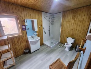 Ein Badezimmer mit Holzwandverkleidung, einer Dusche, Toilette und einem Waschbecken sowie einem Fenster.