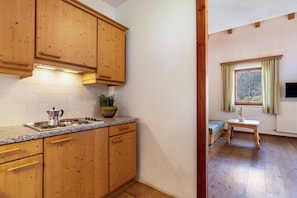A kitchen with wooden cabinets, a granite countertop, and a stove. There is a window with curtains and a view of the outdoors. - Apartment 'Peintenhof Typ B2' with Mountain View, Balcony & Wi-Fi (Campo Tures)
