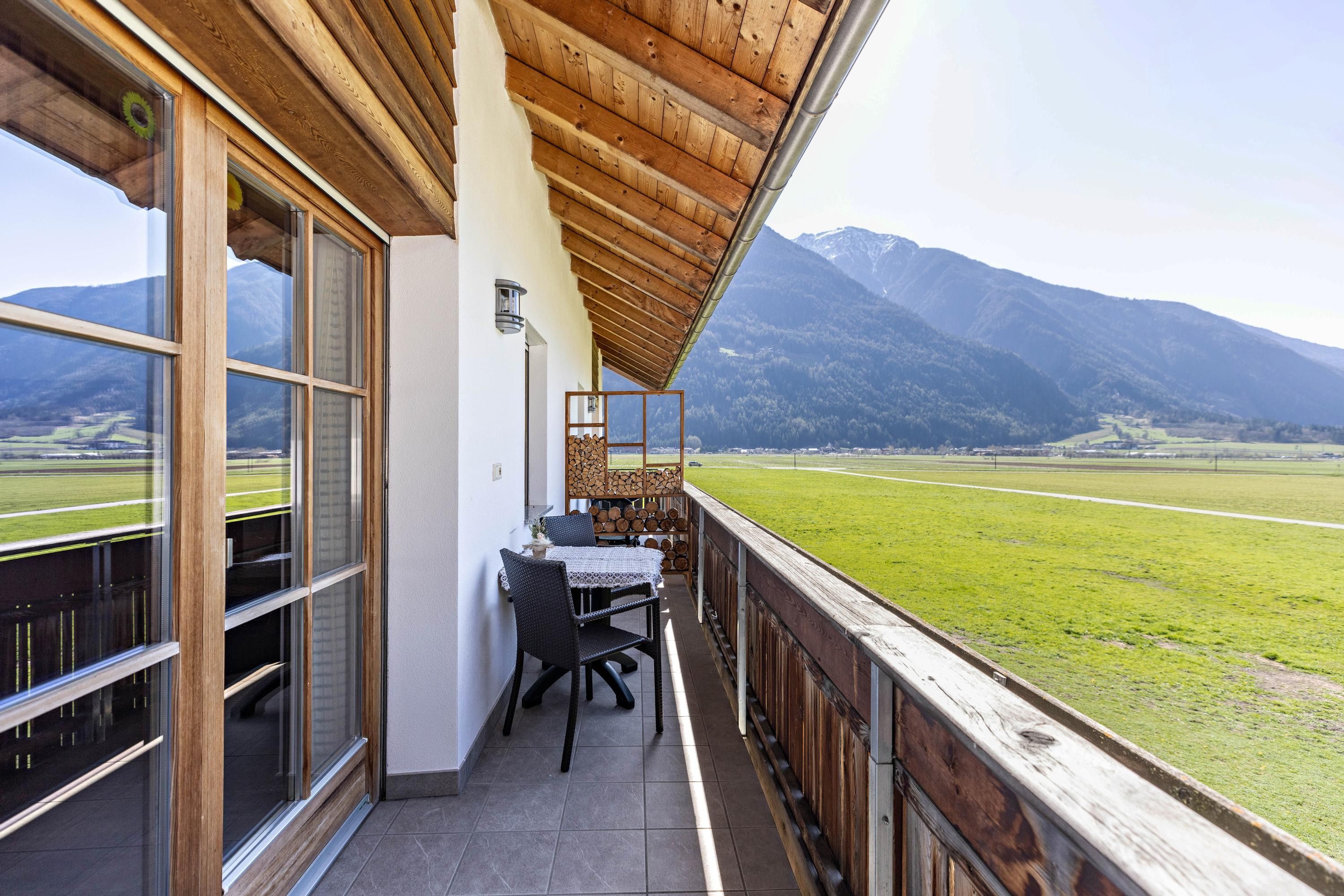 Ein Balkon mit Tisch und Stühlen mit Blick auf ein grünes Feld und Berge.