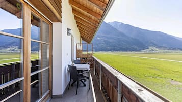 Ein Balkon mit Tisch und Stühlen mit Blick auf ein grünes Feld und Berge.