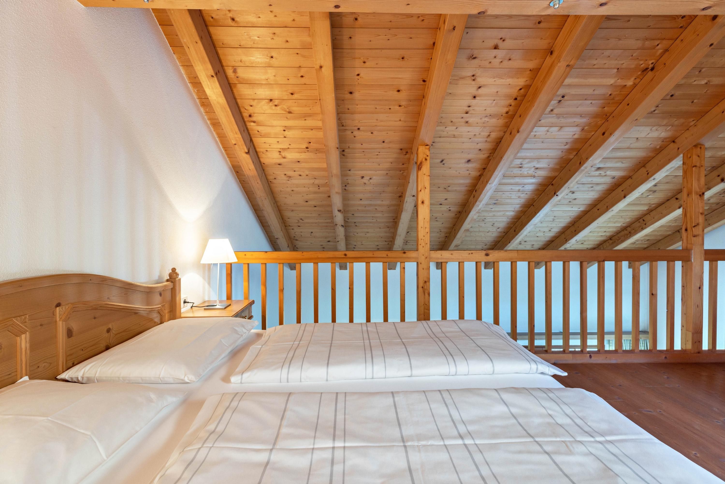 Un dormitorio con techo de madera, una cama con ropa de cama blanca y una mesita de noche con una lámpara.
