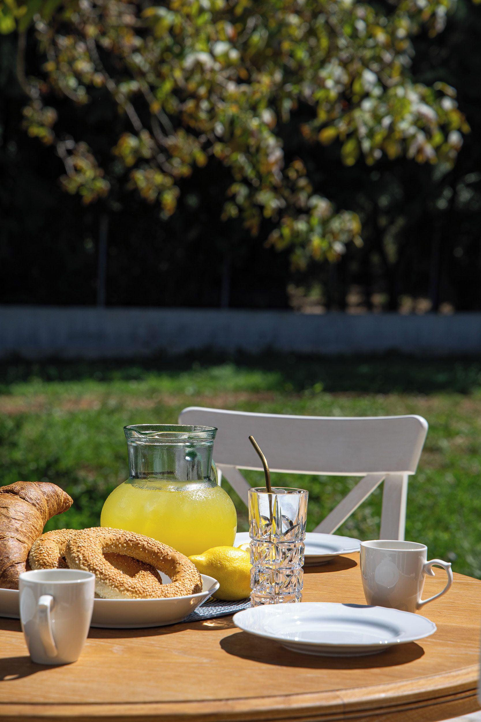 Una mesa de desayuno con croissants, un vaso de jugo, un vaso con popote y una taza blanca.