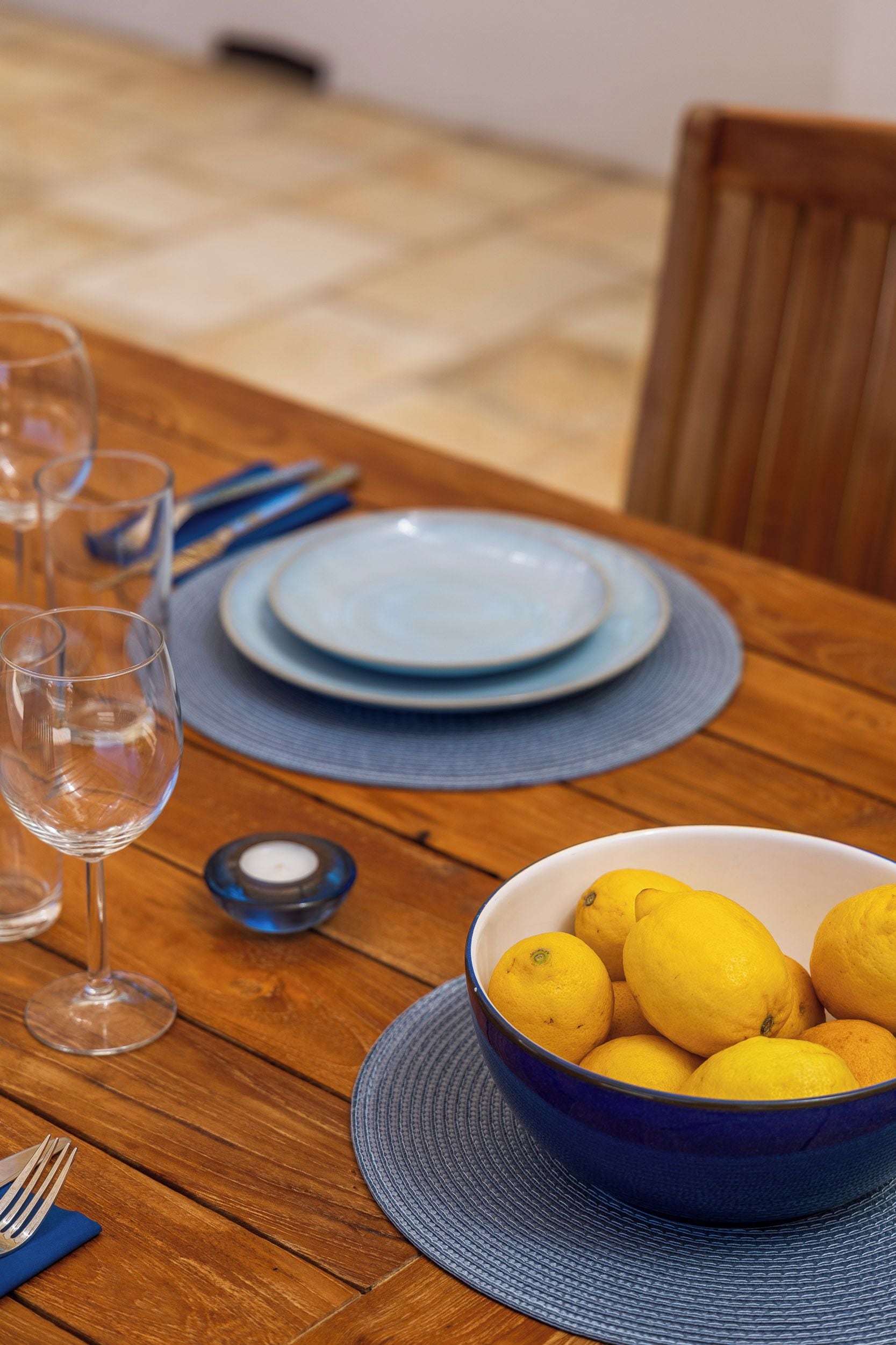 A dining table with a bowl of lemons, a wine glass, and plates.