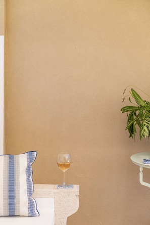 A room with a beige wall, a white table with a glass of white wine, a striped pillow, and a green plant. - Villa Botanica (Corfu)
